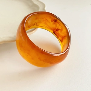 Close-up of a wide amber resin geometric round bangle with translucent sand texture