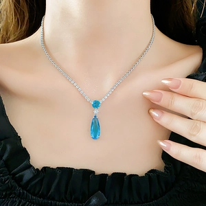 Detail of silver necklace with blue teardrop zircon pendant on a female model