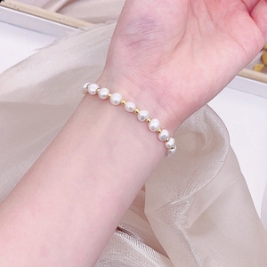 Detailed shot of elegant freshwater pearl and gold bead bracelet on wrist over pink silk