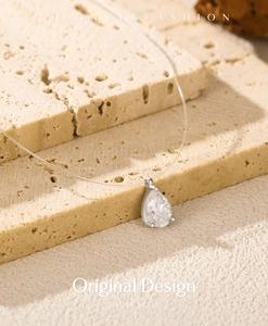 Macro detail of tear-drop moissanite pendant on invisible nylon thread over beige stone