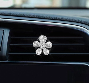 Macro shot of silver crystal flower car air vent clip mounted on a black dashboard vent