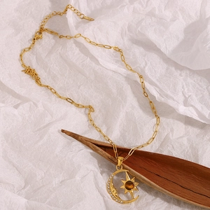 Detail view of 18K gold plated necklace with moon and sun pendant on a vintage paper background