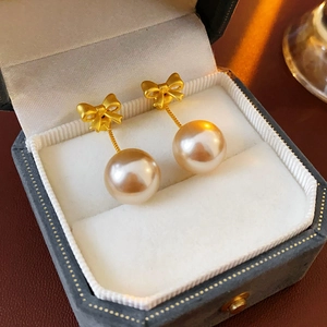 Macro shot of gold bow and pearl earrings displayed in a luxury jewelry gift box