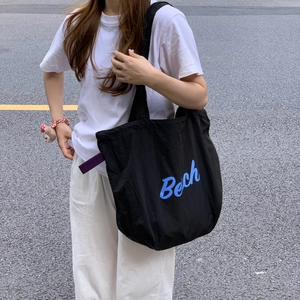 Street style shot of a black nylon tote bag with blue Bech lettering on a model