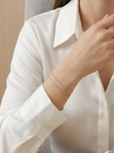 Detail showing elegant layered silver snake chain and bead bracelet on a woman's wrist