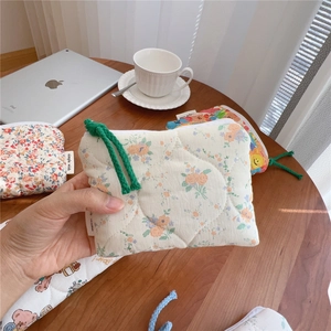 Quilted floral fabric coin purse with green cotton rope zipper pull held over a table