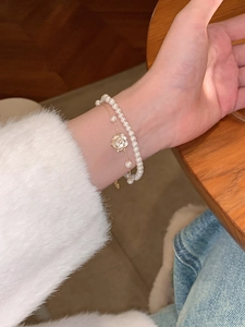 Primer plano de una elegante pulsera de doble capa con colgante de camelia y perlas