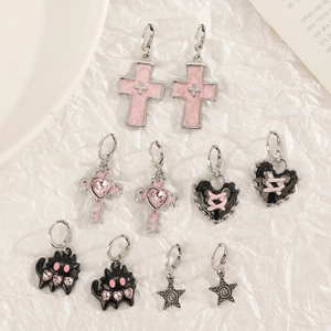 Detailed view of silver cross earrings with pink enamel and black heart pendants on white fabric