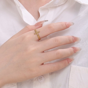 Close-up of minimalist gold-plated adjustable cross ring worn on index finger