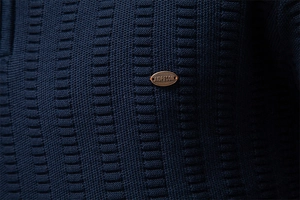 Close-up of bronze metal brand logo on dark blue striped jacquard knit sweater texture