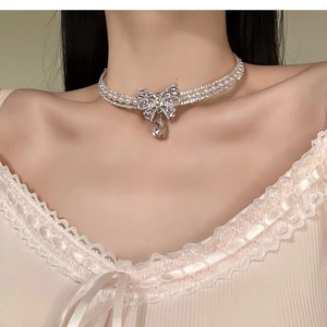 Close-up of double-layer pearl choker with diamond bow and teardrop pendant on neck