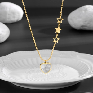 Gold beaded chain necklace with heart shell pendant and three star charms on white ceramic