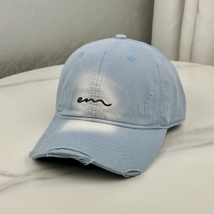 Close-up of distressed light blue cotton baseball cap with embroidered brown 'em' logo
