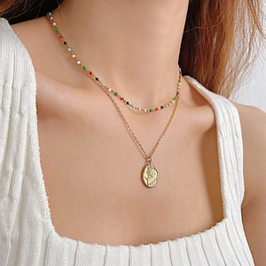 Détail d'un collier doré double épaisseur avec pendentif rose et perles colorées