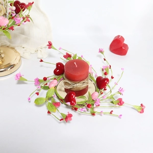 Close-up of red pillar candle with heart berry wreath on a wooden base for table decor