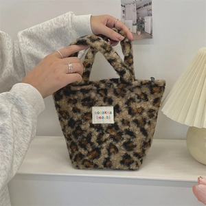 Detail of leopard print plush handbag showing soft texture and logo label on a desk
