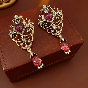 Detail of vintage gold earrings with pink teardrop crystals on a brown leather case