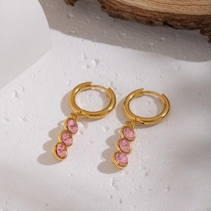 Detail of gold hoop earrings with three pink oval zircons on a white textured background