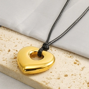 Polished golden heart pendant on black wax cord resting on a natural stone surface