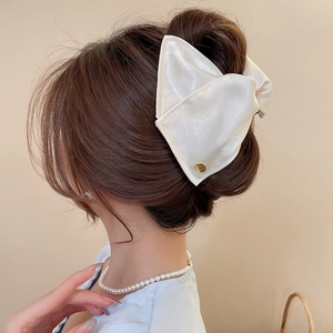 Detail of a large cream satin bow hair claw clip showing luxurious silk fabric texture