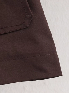 Detailed view of dark brown double-stitched seams and twill texture on short trench coat