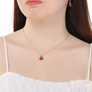 Close-up of cherry jewelry set featuring red enamel cherry necklace and matching earrings