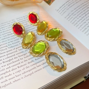 Detail of vintage gold-rimmed earrings with oval red and green gems on a book page