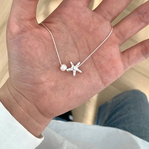 Detailed view of silver starfish pendant and round pearl on a delicate necklace chain