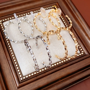 Detail view of C-shaped metal earrings with diamond-cut texture and resin clips for non-pierced ears