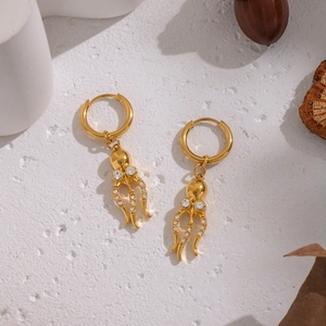 Goldene Oktopus-Ohrringe mit Zirkonia auf weißer Oberfläche mit natürlicher Dekoration