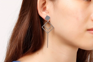 Detail of hollow geometric diamond long drop earrings worn by a model in silver metal