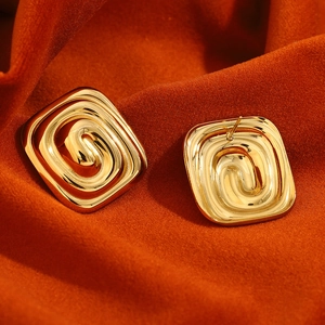 Gros plan de boucles d'oreilles carrées labyrinthe dorées sur tissu plissé orange