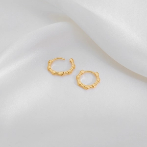 Detailed view of gold-tone bamboo texture hoop earrings on white silk fabric background