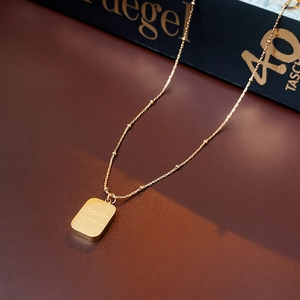 Close-up of golden titanium steel square pendant necklace with engraved letters on bead chain