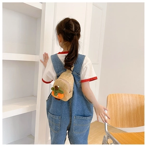 Detail of hand-woven straw bag with cute carrot decor on child's back with blue denim