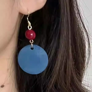 Gros plan de boucles d'oreilles rétro en acrylique bleu avec perle rouge sur l'oreille.