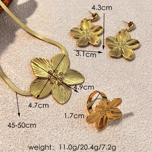 Golden flower jewelry set with necklace earrings and ring on a beige textured background