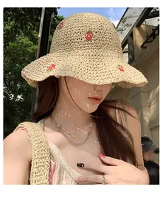 Detail of hand-woven straw bucket hat with red strawberry embroidery and natural wavy brim