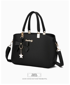 Side view of black lychee grain leather handbag with gold hardware and floral pendant