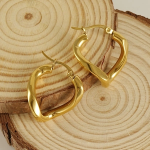 Irregular heart-shaped gold twisted earrings on a rustic wood background
