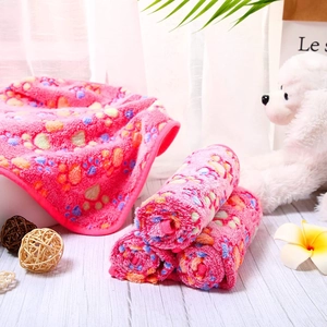 Pink coral fleece pet blanket with colorful paw prints on a warm wooden floor