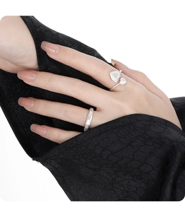 Detail of silver rings featuring geometric facets and heart shapes on textured black fabric