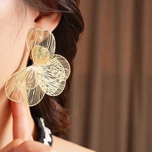 Détail de boucles d'oreilles dorées ajourées en forme de fleur portées par un mannequin