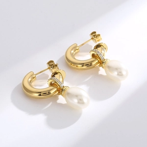 Détail d'une boucle d'oreille C dorée avec perle blanche et accents de cristal