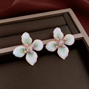 Macro shot of floral earrings with white enamel petals and champagne crystal center