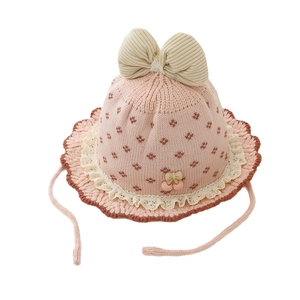 Rosa gestrickter Babyhut mit beiger Schleife und Kirsch-Anhängern auf weißem Grund