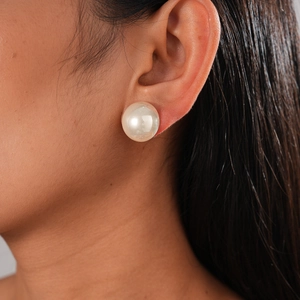 Close-up of a large white faux pearl stud earring worn on the ear showing elegant luster