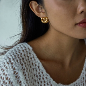 Close-up of a model wearing gold 18K stainless steel pretzel heart-shaped stud earrings