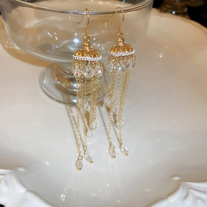 Detail of elegant gold tassel earrings with crystal beads hanging on glass rim
