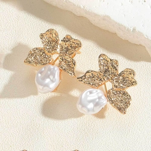 Detail of floral gold earrings with white pearls on a textured stone surface